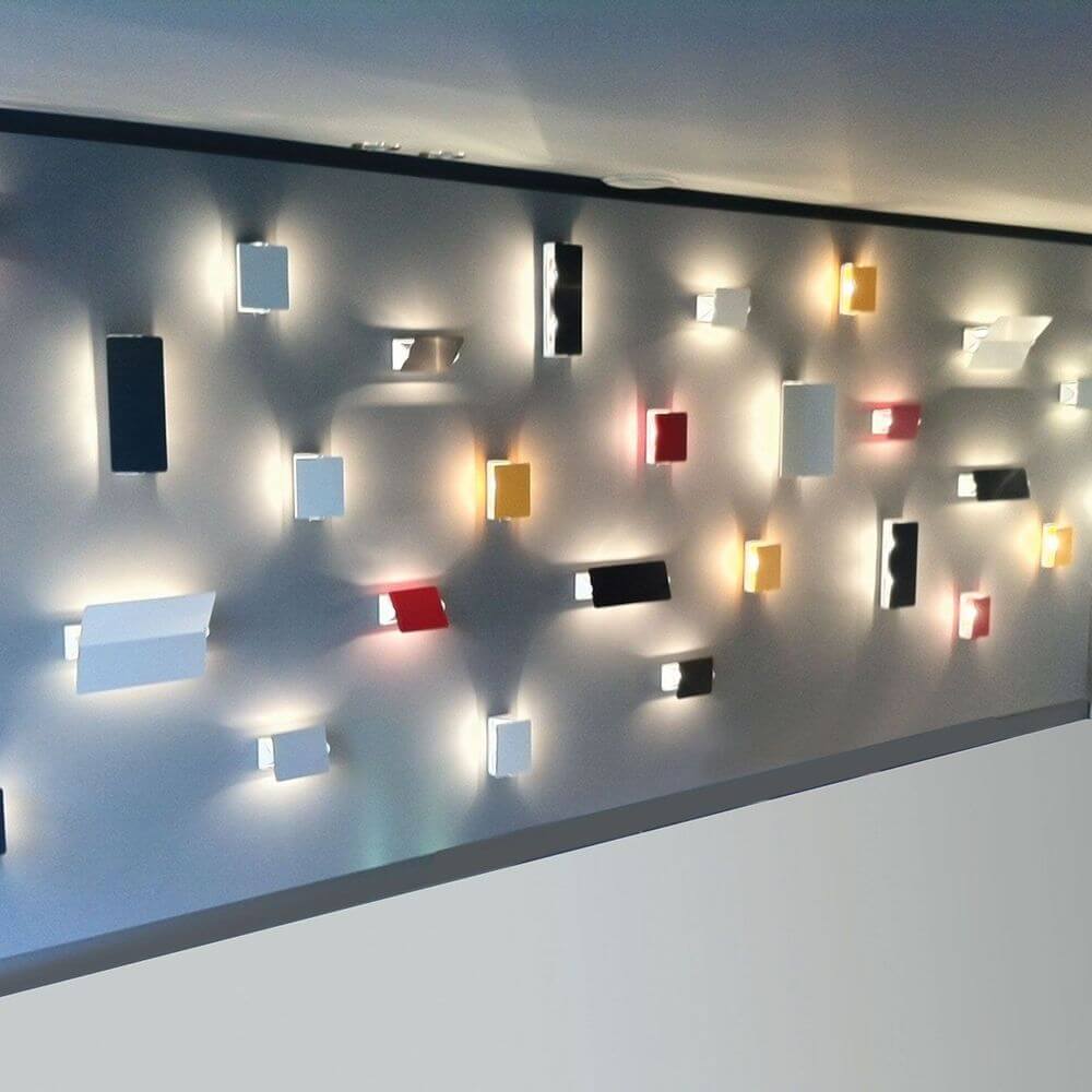 Nemo Applique À Volet Pivotant Plié LED Wandlampe 26x34 an einer Wand mit verschiedenen Farben und Formen.