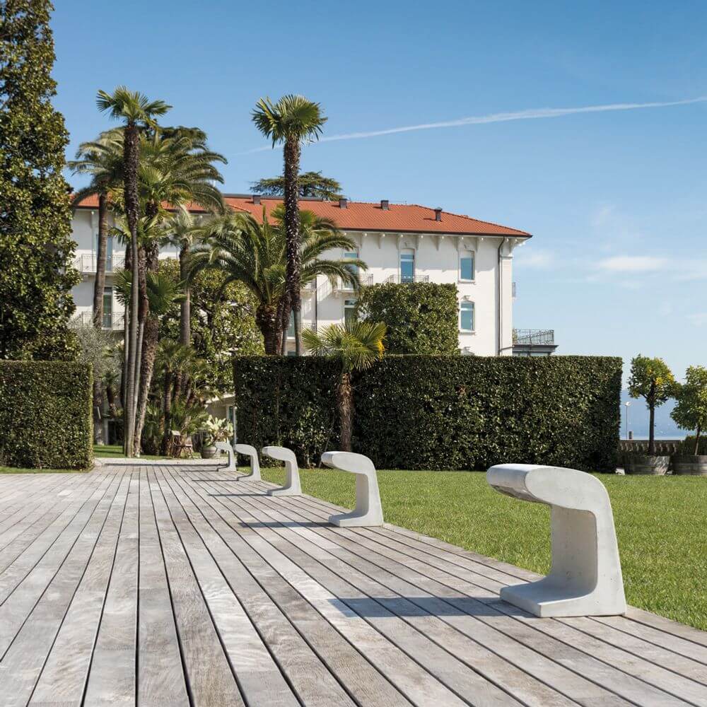 Nemo Borne Béton Grande Outdoor LED Stehlampe IP44 auf einem Holzdeck mit Palmen und einer luxuriösen Villa im Hintergrund.