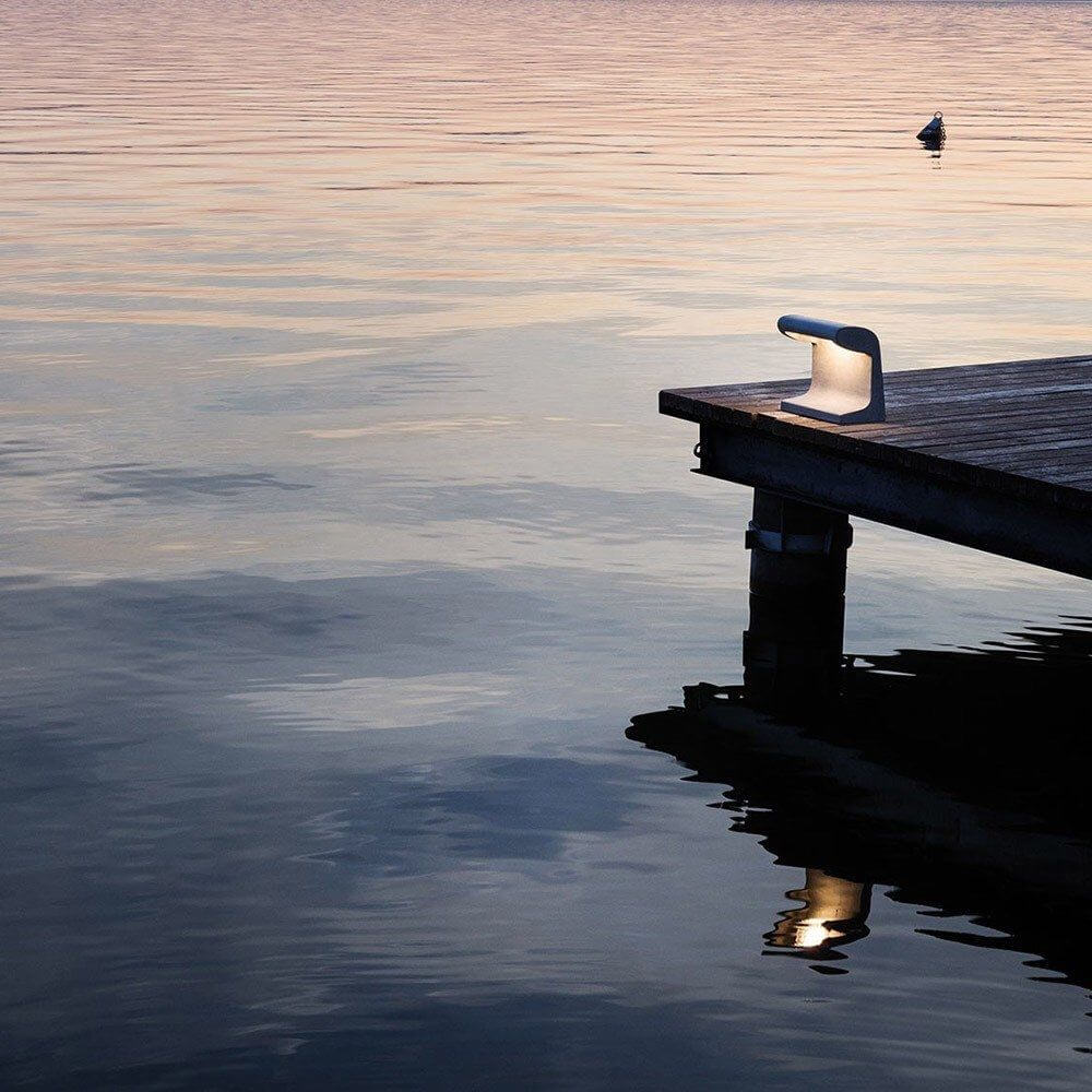 Nemo Borne Béton Petite Outdoor LED Tischlampe IP44 neben einem Holzsteg im Wasser reflektiert bei Sonnenuntergang