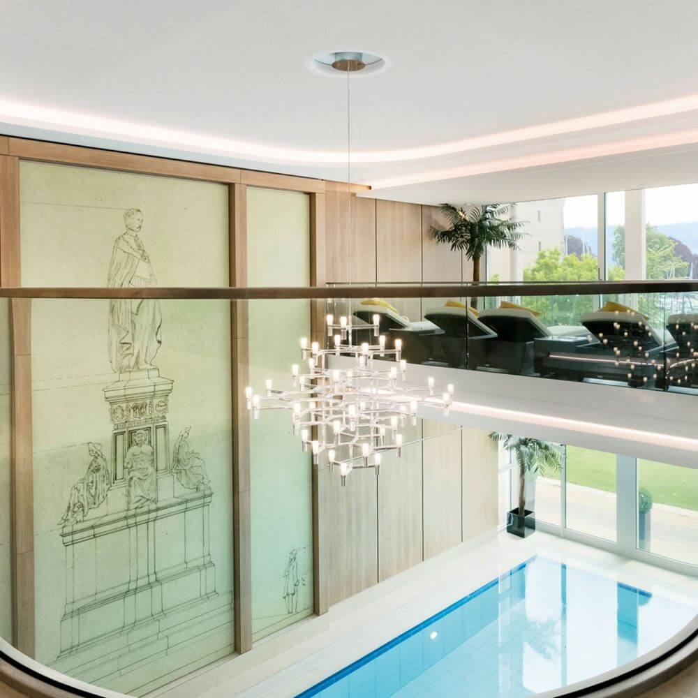 Moderne Wohnung mit Nemo Crown Magnum Kronleuchter, Schwimmbecken, und eleganter Holzverkleidung im Hintergrund.