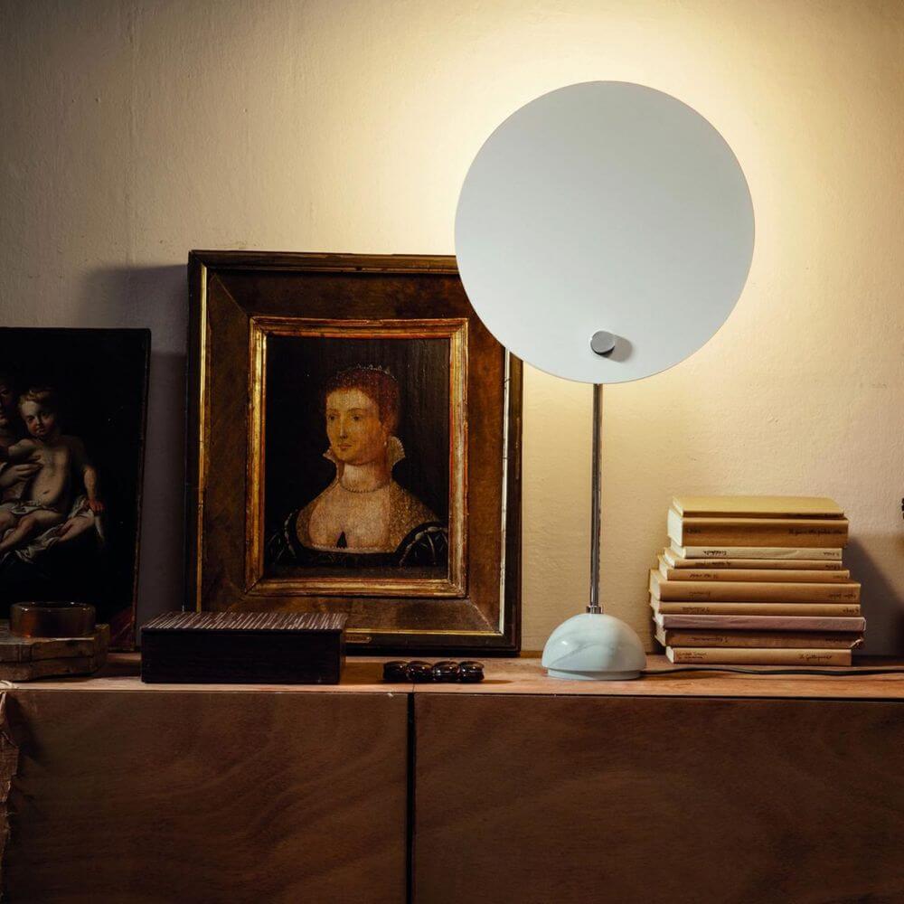 Nemo Kuta Tischlampe für indirektes Licht auf einem Tisch, beleuchtet Kunstwerke und Bücher.