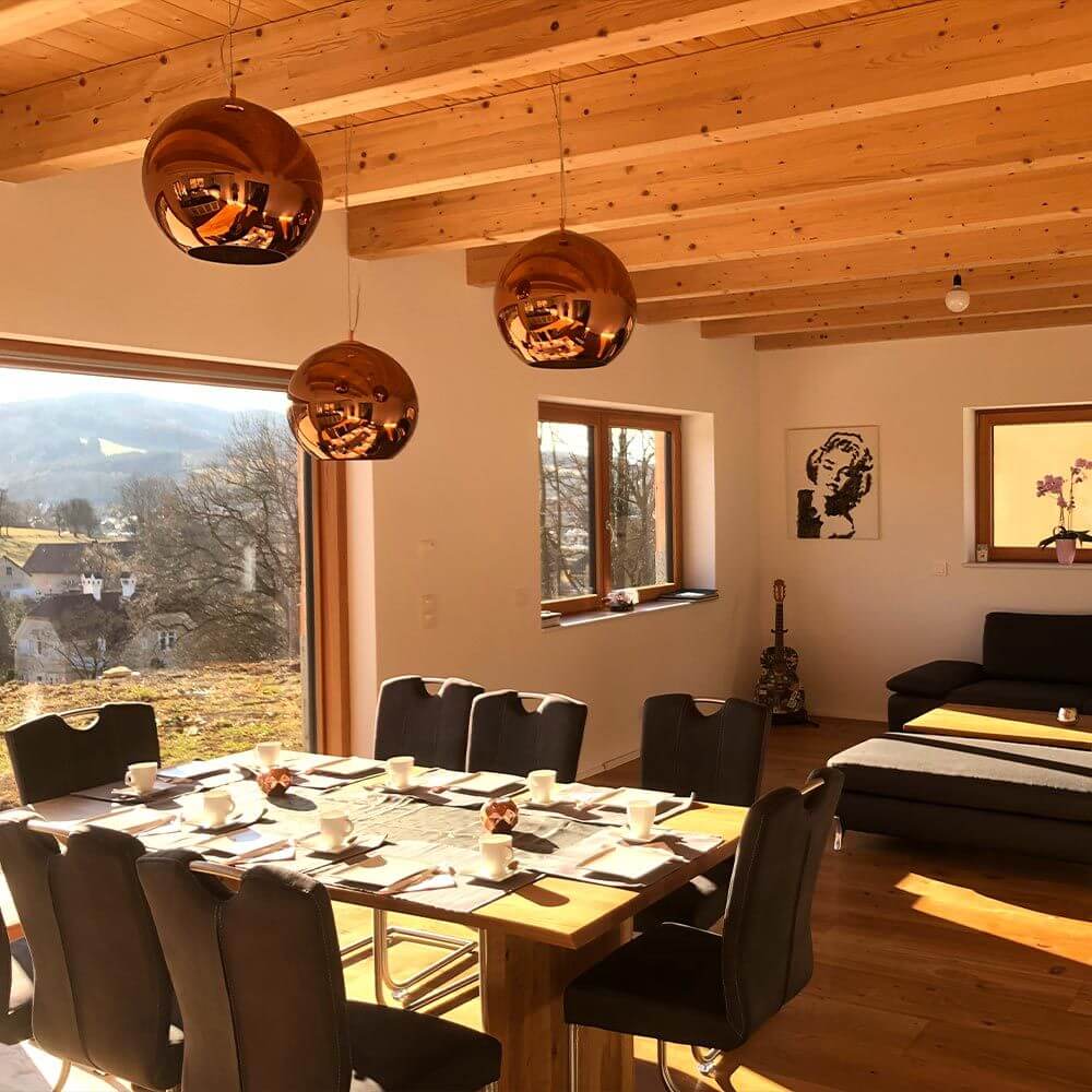 Pendelleuchten aus Kupfer in einem modernen Essbereich mit Holzdecke und großem Fenster.