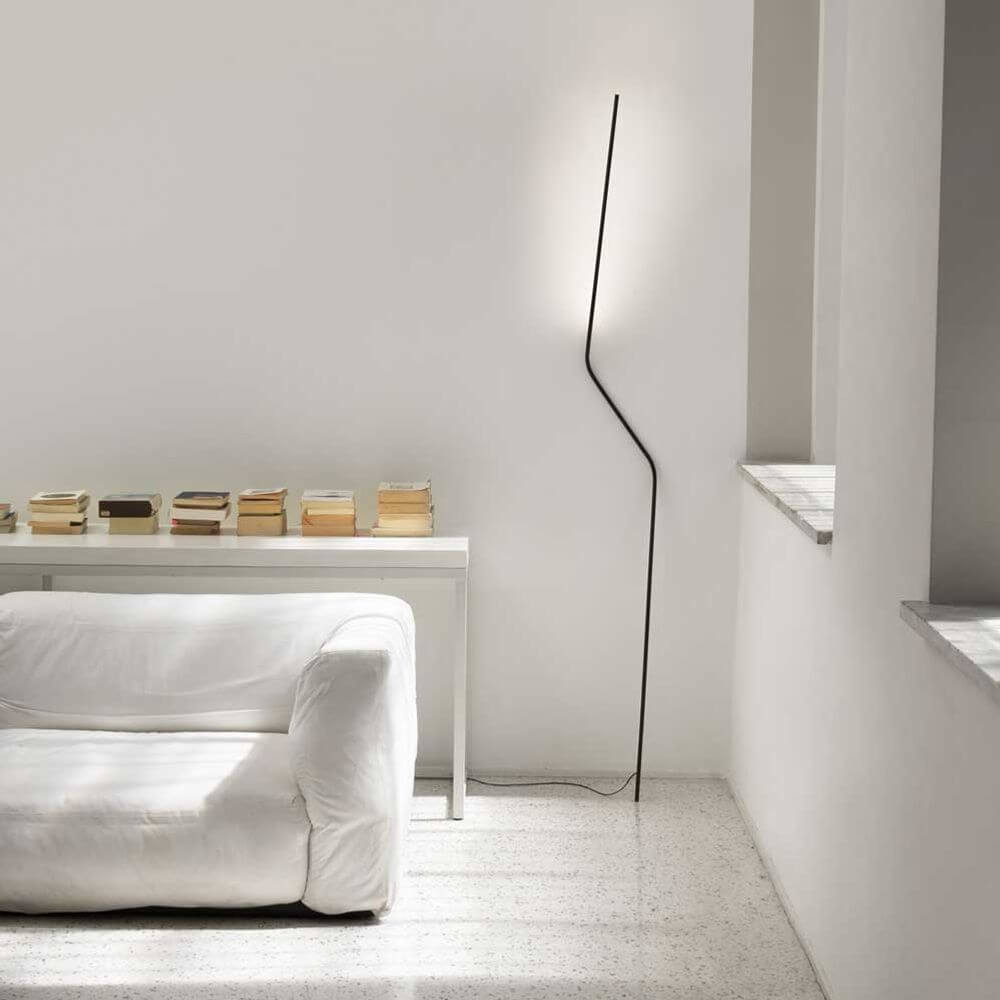 Nemo Neo LED Stehlampe zum anlehnen in modernem Wohnambiente mit weißem Sofa und Bücherstapel.