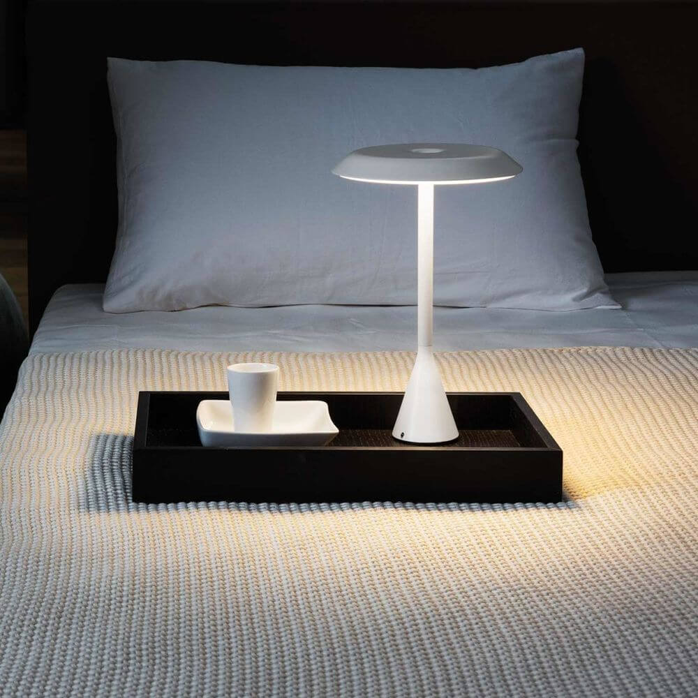 Nemo Panama Mini LED Akku-Tischlampe 30cm auf einem Nachttisch neben einer Tasse und einem kleinen Teller.