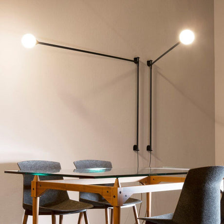 Nemo Potence Pivotante wall lamp 200cm on a wall above a table with modern chairs.