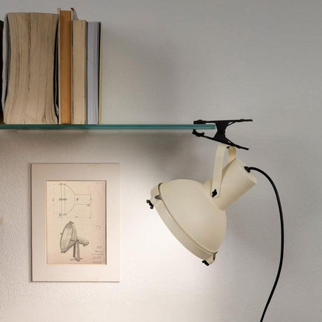 Nemo Projecteur 165 Klemmleuchte an einem Regal mit Büchern und einer Zeichnung im Hintergrund.