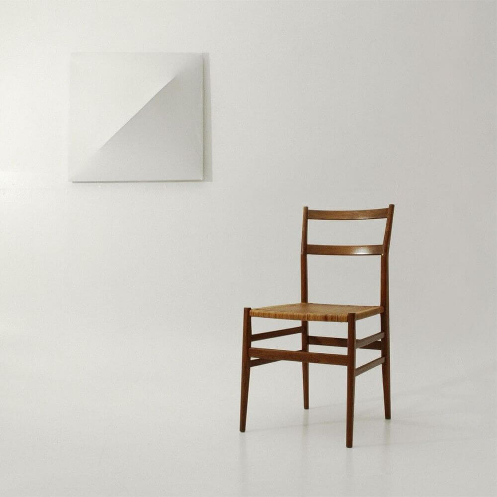 Schlichte Holzstuhl vor minimalistischer Wandgestaltung mit geometrischem Kunstwerk.