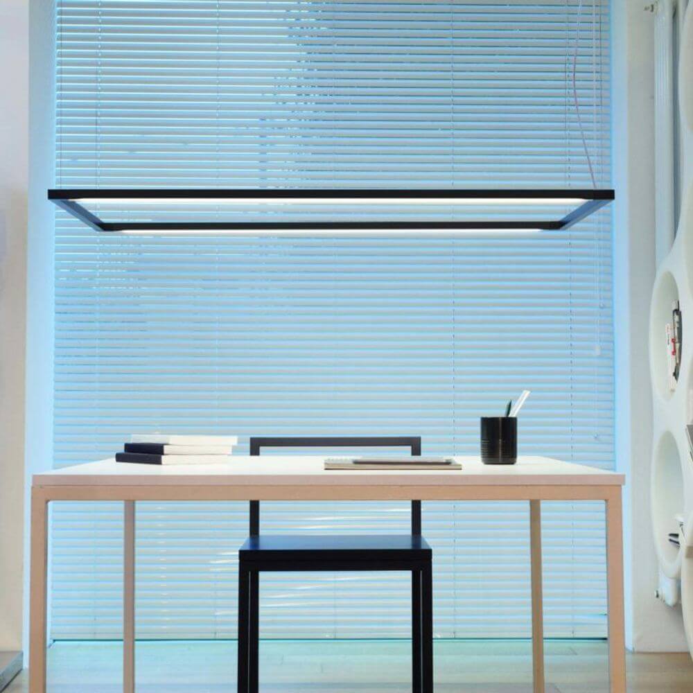 Nemo Spigolo Horizontal LED Hängeleuchte drehbar über einem minimalistischen Schreibtisch mit Holzoberfläche.