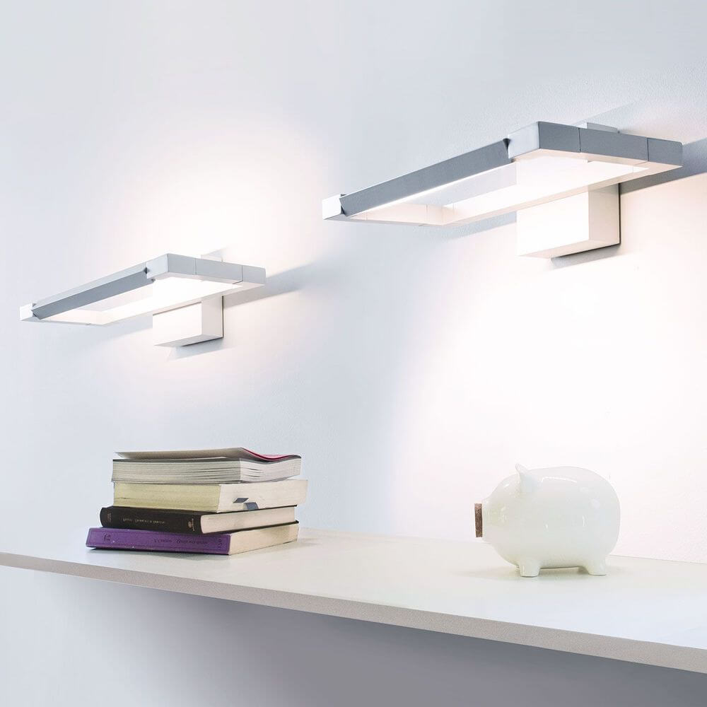 Nemo Spigolo LED Wandleuchte 360° drehbar an einer Wand über einer Ablage mit Büchern und einem Sparschwein.