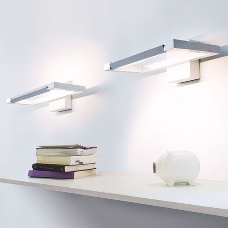 Applique Nemo Spigolo LED orientable à 360° sur un mur au-dessus d’une étagère avec des livres et une tirelire.