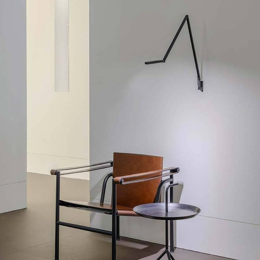 Nemo Untitled LED Wandleuchte in modernem Design, vormontiert über einem eleganten Stuhl und Tisch in minimalistischer Umgebung.