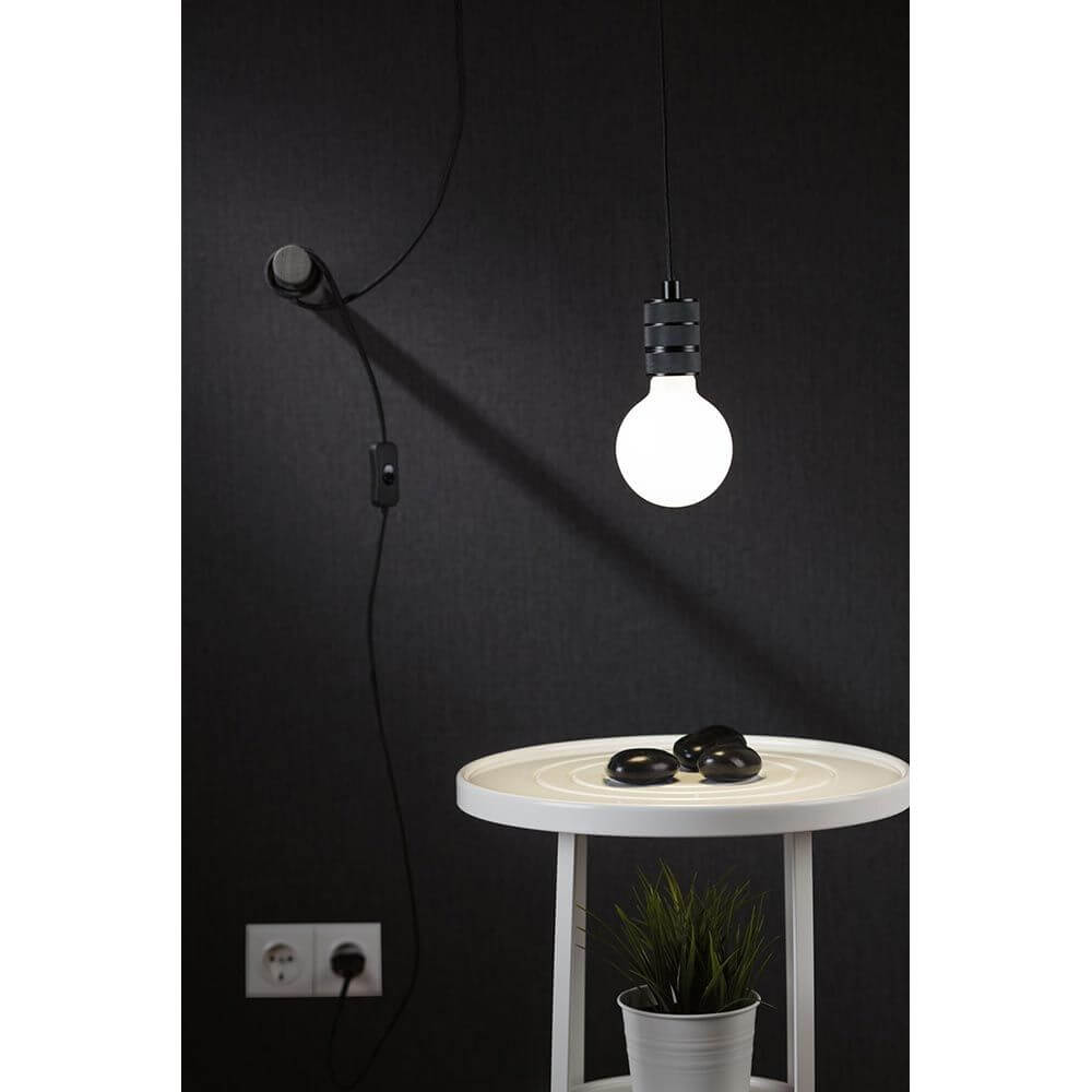 Pendelleuchte Tilla in Schwarz mit E27 Leuchtmittel über einem Tisch, dekoriert mit Pflanzen und Steinen.