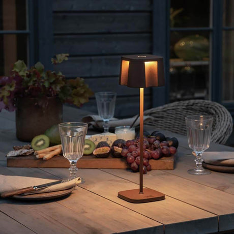 Nice LED Outdoor USB-Tischlampe CCT auf einem Tisch, beleuchtet und umgeben von Essen und Getränken.