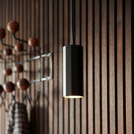 Alanis Pendelleuchte: stilvolle, minimalistische Pendelleuchte mit 10-seitigem Profil, hängend an einer Holzwand.