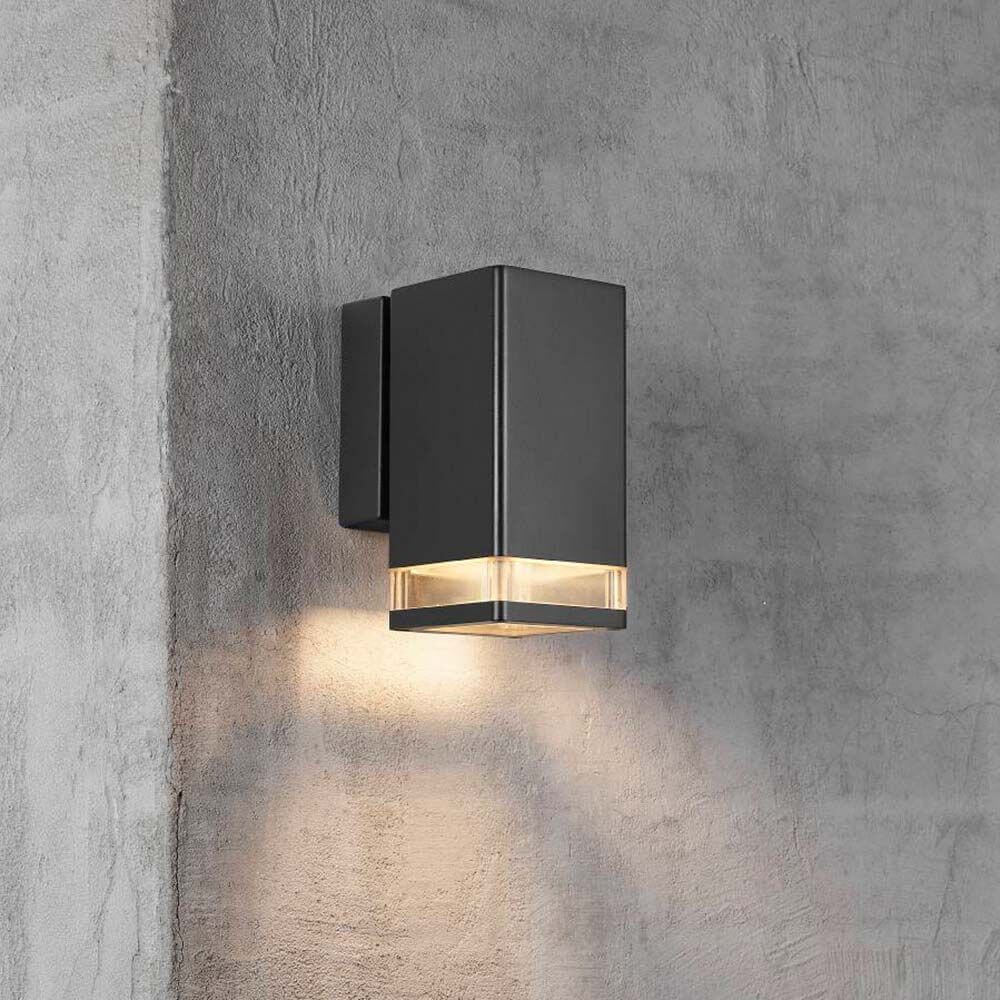 Außen-Wandlampe Elm IP44 Schwarz, Klar an einer Wand montiert mit warmem Licht.