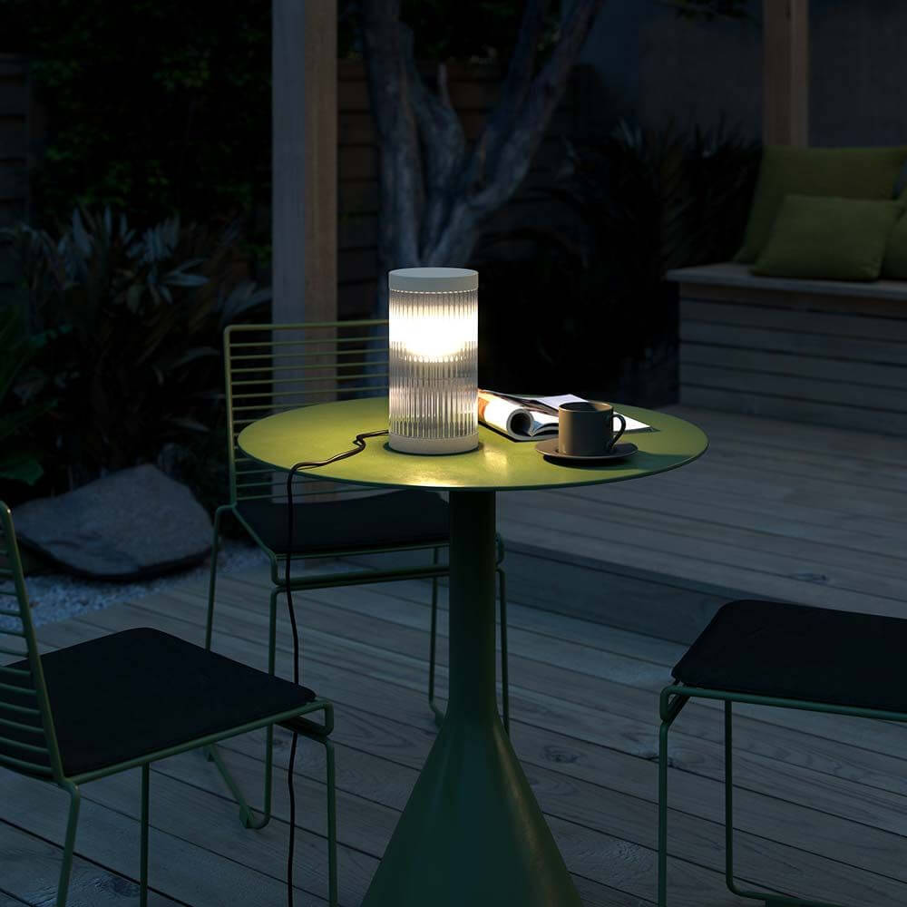 Coupar Tischleuchte auf einem grünen Tisch im Freien, ideal für abendliche Entspannung.