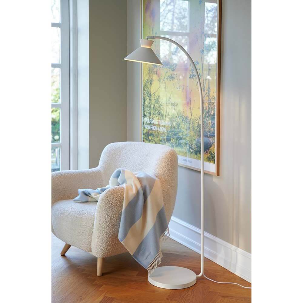 Dial Stehleuchte Weiß neben einem bequemen Sessel in einem modernen Wohnzimmer, mit einem dekorativen Uplight-Effekt.