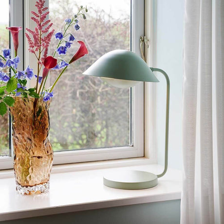 Lampe de table Freya au design scandinave à côté d’un vase avec des fleurs colorées sur un rebord de fenêtre.