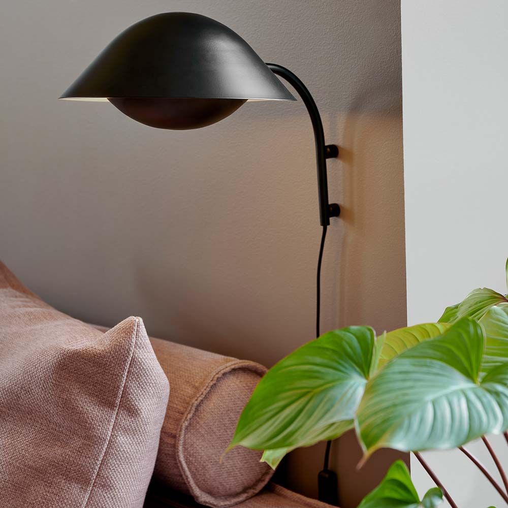 Freya Wandleuchte mit skandinavischem Design, stilvoll an der Wand montiert, neben einem Sofa und einer Pflanze.