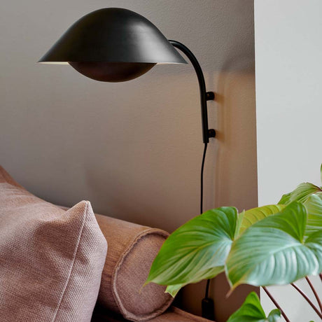 Freya wall light with Scandinavian design, stylishly mounted on the wall, next to a sofa and a plant.