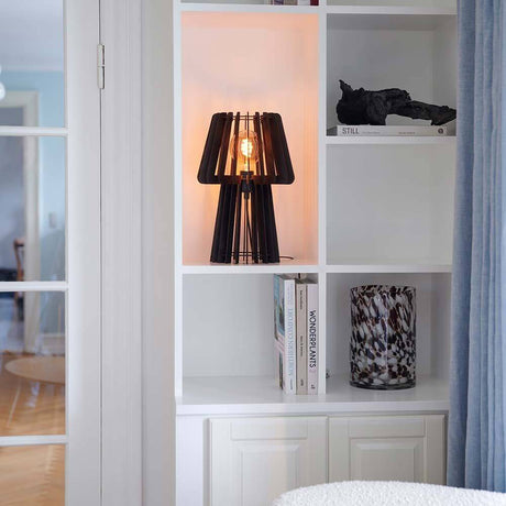 Lampe de table Groa en bois sur une étagère, crée une lumière chaude et des ombres dans la pièce.