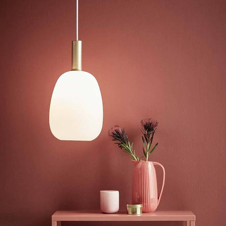 Suspension Alton 23 blanc, blanc opale au-dessus d’une table avec un vase rose et des plantes devant un mur rouge.