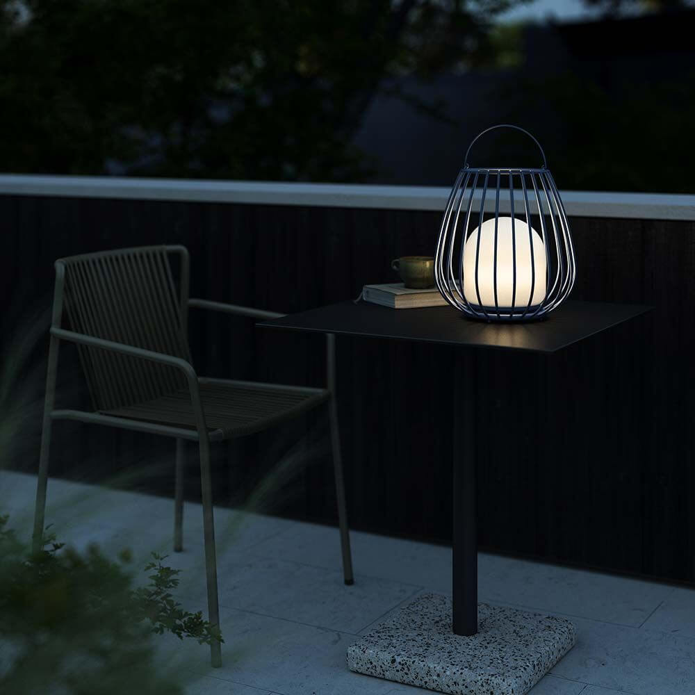 Die Jim To Go LED Akku Bodenleuchte von Says Who auf einem Tisch im Freien, perfekt für stimmungsvolle Beleuchtung.