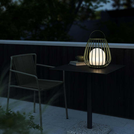 Jim To Go LED rechargeable floor lamp IP54 on a table outdoors, surrounded by plants and a chair.