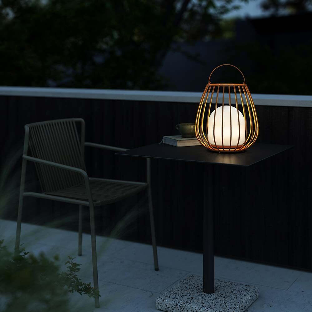 Jim To Go LED Akku Bodenleuchte auf einem Tisch auf einer Terrasse, umgeben von Natur bei Dämmerung.