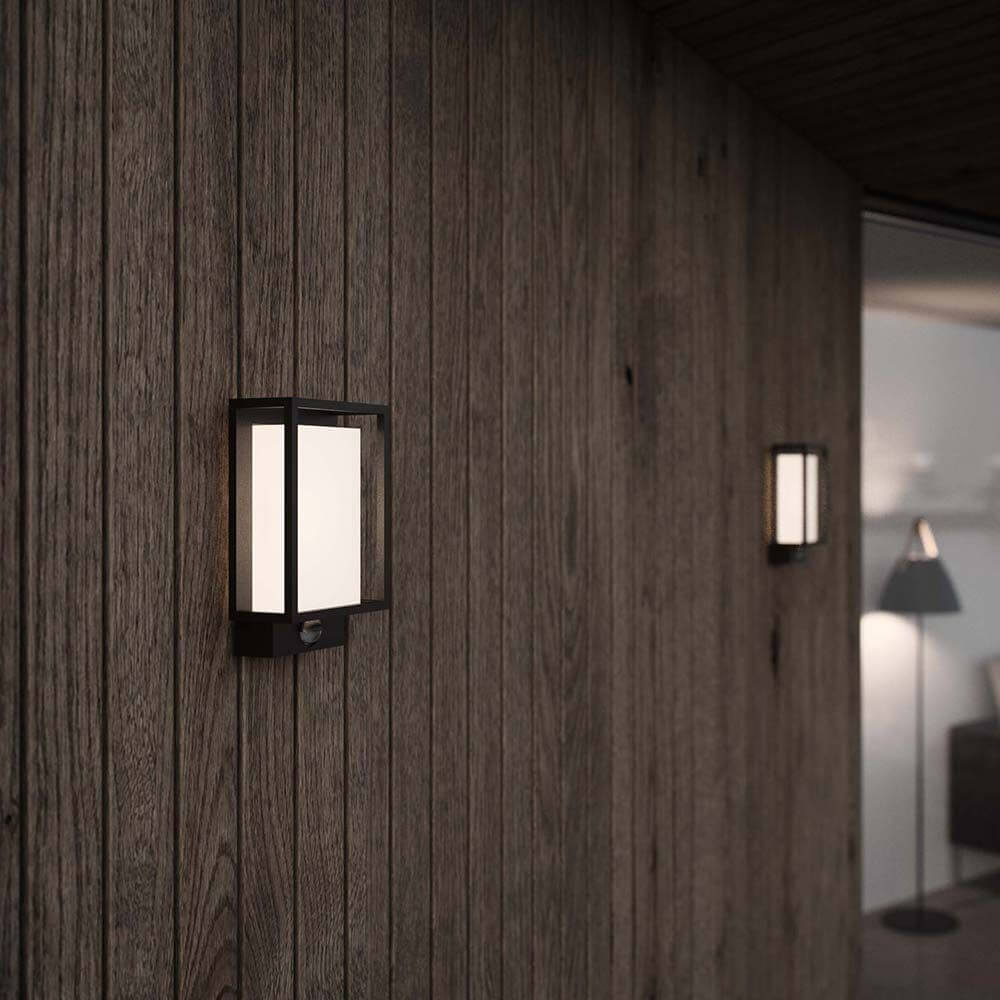 LED-sensorvegglampe Nestor IP44 dimbar svart montert på en trevegg.