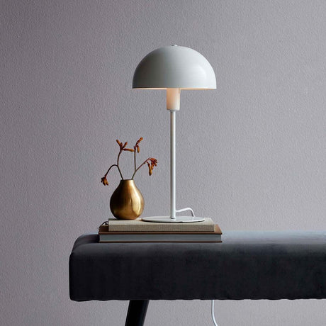 Bordlampe Ellen Hvit på et bord med bok og vase, minimalistisk skandinavisk design.