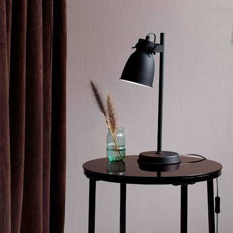 Lampe de table Adrian noire sur une table avec un vase et des plantes décoratives.
