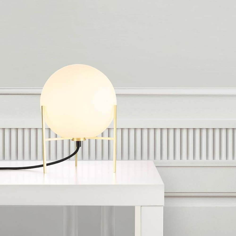 Moderne Tischleuchte Alton in Weiß mit Opalglas und goldenem Gestell auf einem weißen Tisch.