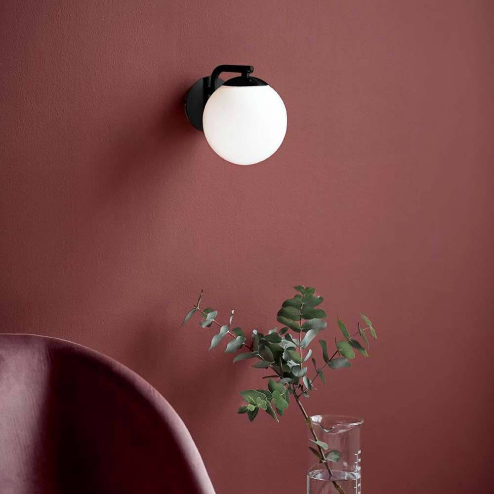 Wandlampe Grant Schwarz, Opal Weiß an einer roten Wand mit Pflanzen im Vordergrund.