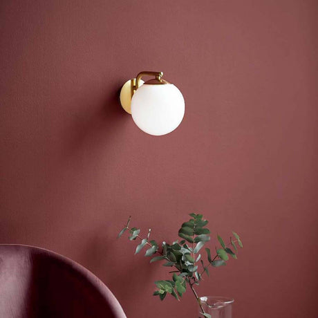 Wandleuchte Grant Messing, Opal Weiß an einer roten Wand mit einer eleganten Glaskuppel.