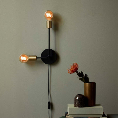 Josefine wall light in black and brass on a wall with modern decorations and plants.