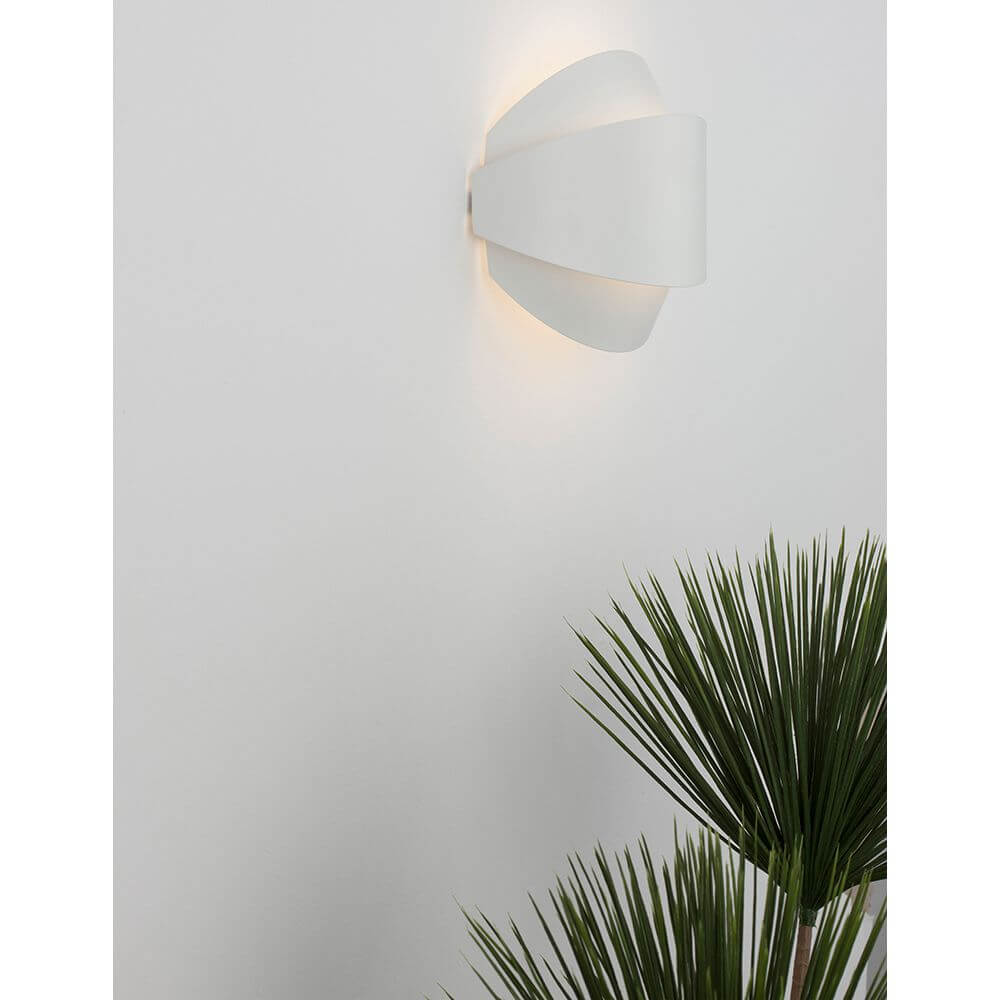 Astrid LED Wandleuchte an einer Wand mit warmweißem Licht und einer Pflanze im Vordergrund.