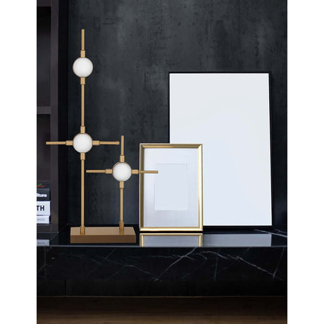 Lampe de table Atomo LED sur une table moderne avec des accents dorés et un cadre vide en arrière-plan.