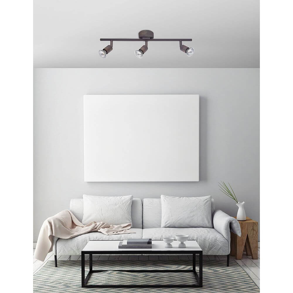 Base Balkenstrahler Metall 3-flammig über einem modernen Wohnzimmer mit Sofa und leerer Wand.