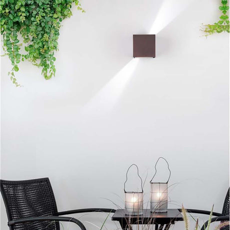 Como LED wall light brown on a wall with plants, illuminating a cozy table.