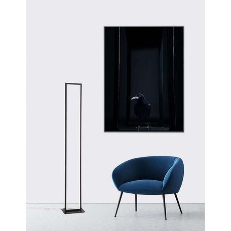 Cornice LED Stehleuchte 153cm Schwarz neben blauer Sitzgelegenheit und Kunstwerk an der Wand.