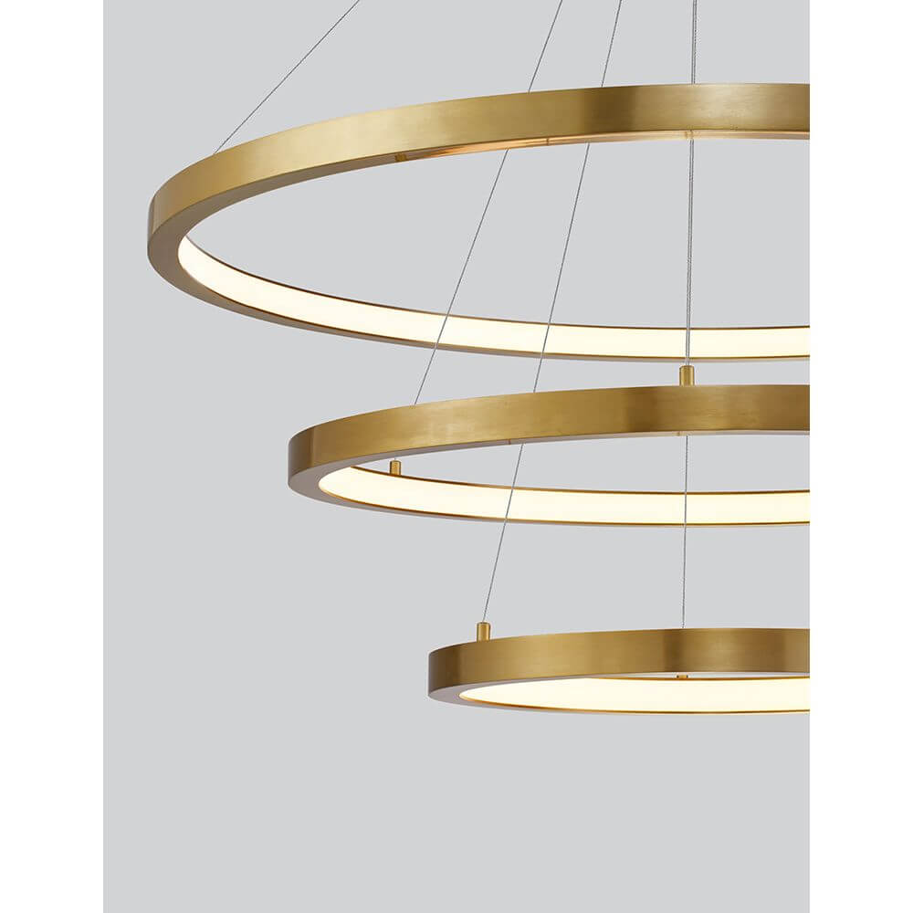 Empatia LED Hängelampe 3 Ringe mit drei goldenen Ringen und warmweißem Licht auf grauem Hintergrund.