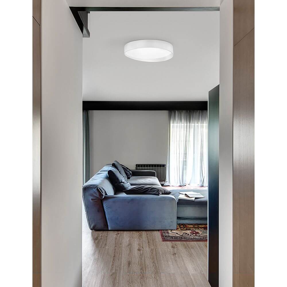 Fano LED Deckenlampe Weiß im modernen Wohnzimmer mit blauer Couch und Fenster.