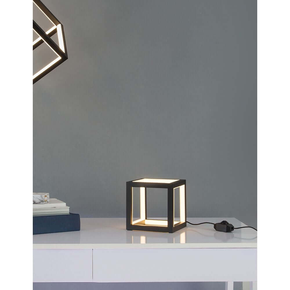 Gabbia LED Würfel Tischlampe auf einem weißen Tisch, modernes Design mit goldenen Akzenten.