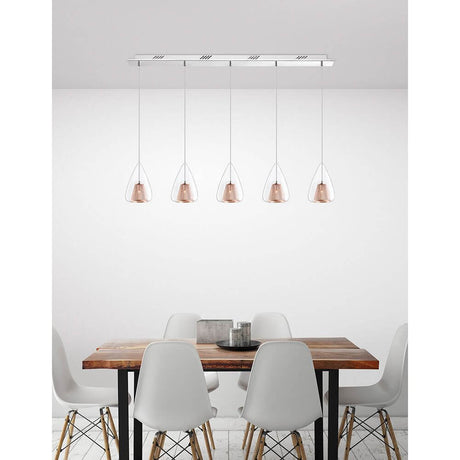 Hugo 5-pære glas pendel, klar, rosa guld over et moderne spisebord med hvide stole.