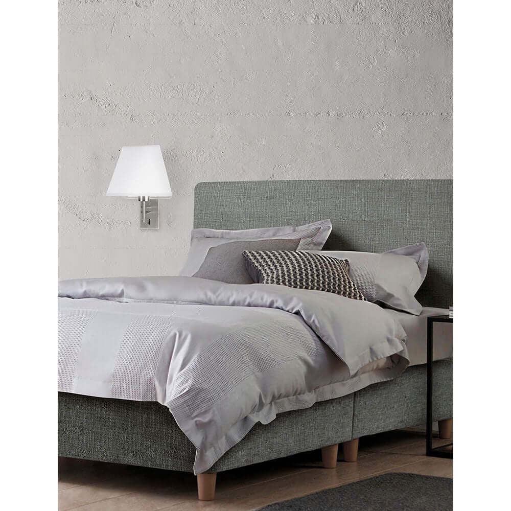 Schlafzimmer mit Logan Wandlampe Metall Textil, grauem Bett und Kissen für modernen Stil.