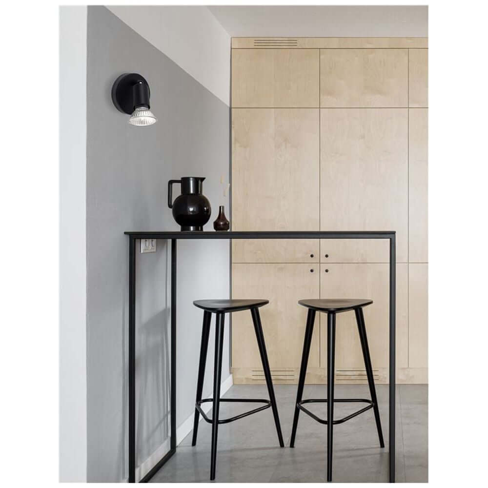 Moderne Lup Spot Wandlampe Metall an einer Wand über einem schwarzen Tisch mit Stühlen.