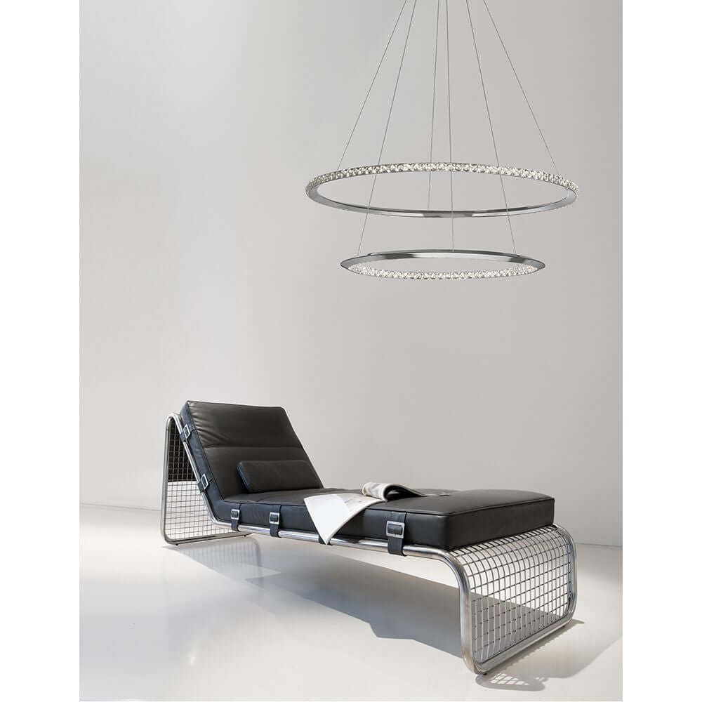 Netuno LED Kristall Hängelampe Ø 80cm über einem modernen schwarzem Lounge-Sessel auf einem weißen Boden.