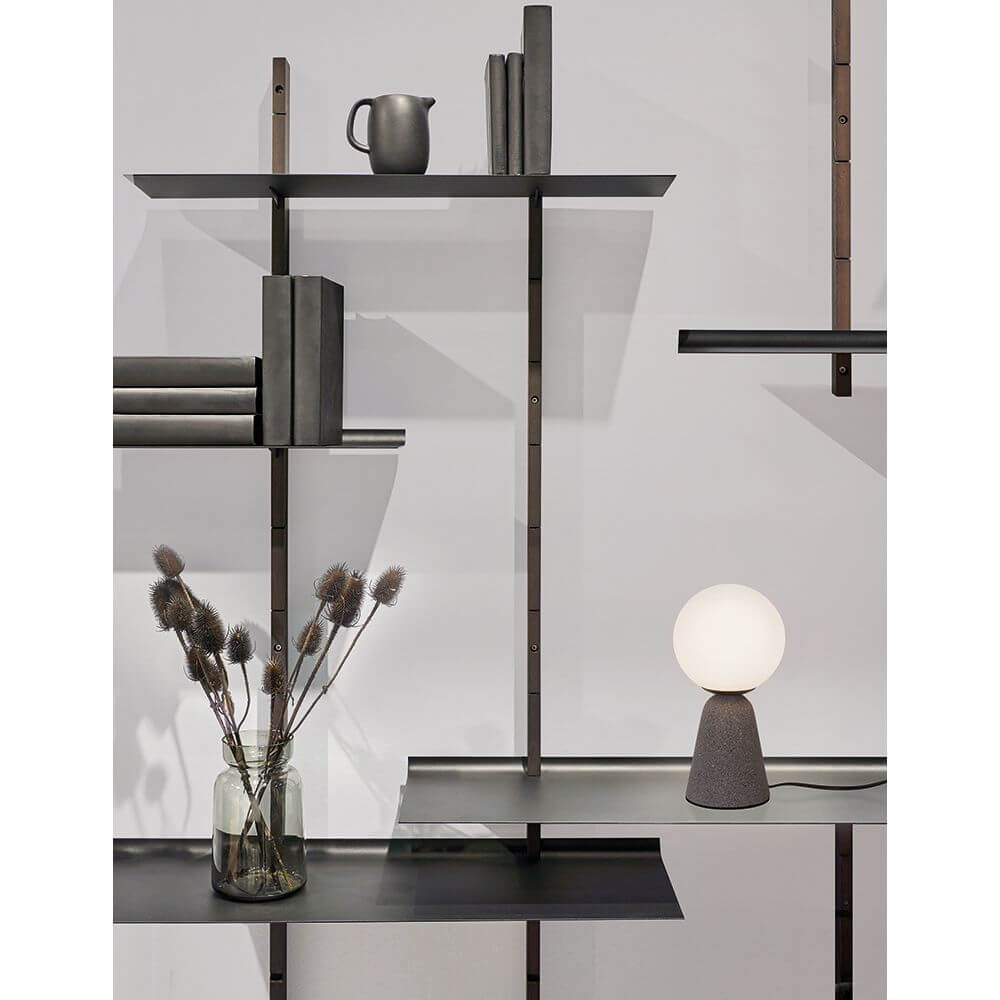 Orion Tischleuchte Beton auf einem modernen Regal mit Büchern und einer Vase.