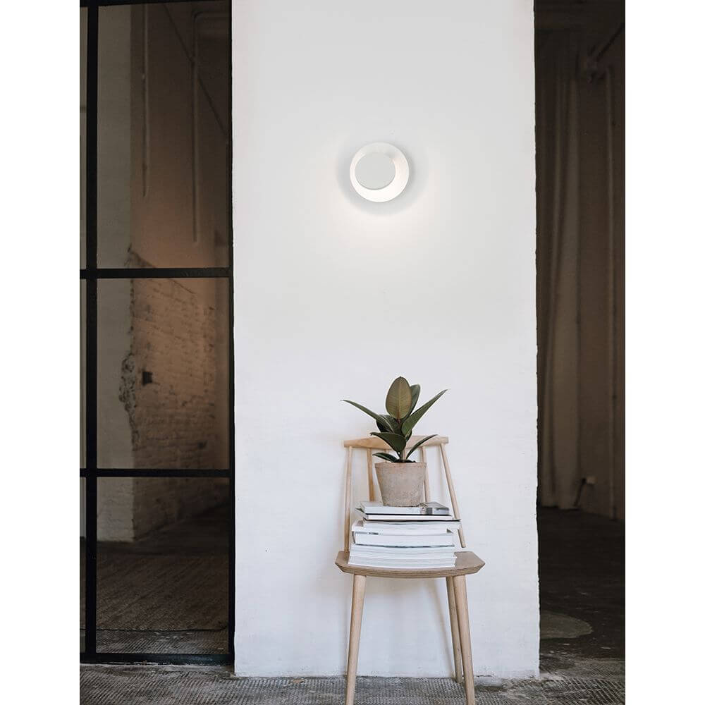 Otto LED Wandlampe Ø 12cm Weiß an Wand mit Pflanze auf Stuhl im modernen Innenraum.